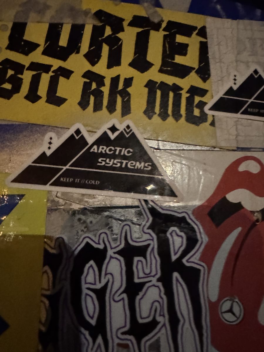 An Arctic Systems sticker among layers of stickers on a wall
